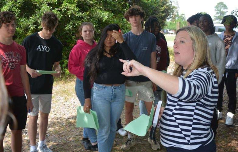 Teacher pointing to something in the distance and students standing around her watching.