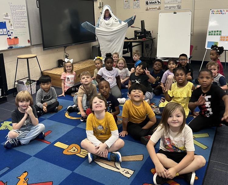 A teacher dressed up as a shark stands behind a class of students