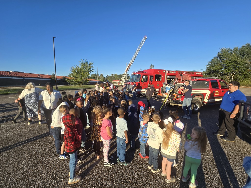 Students and teachers standing in front of fire trucks and firemen.