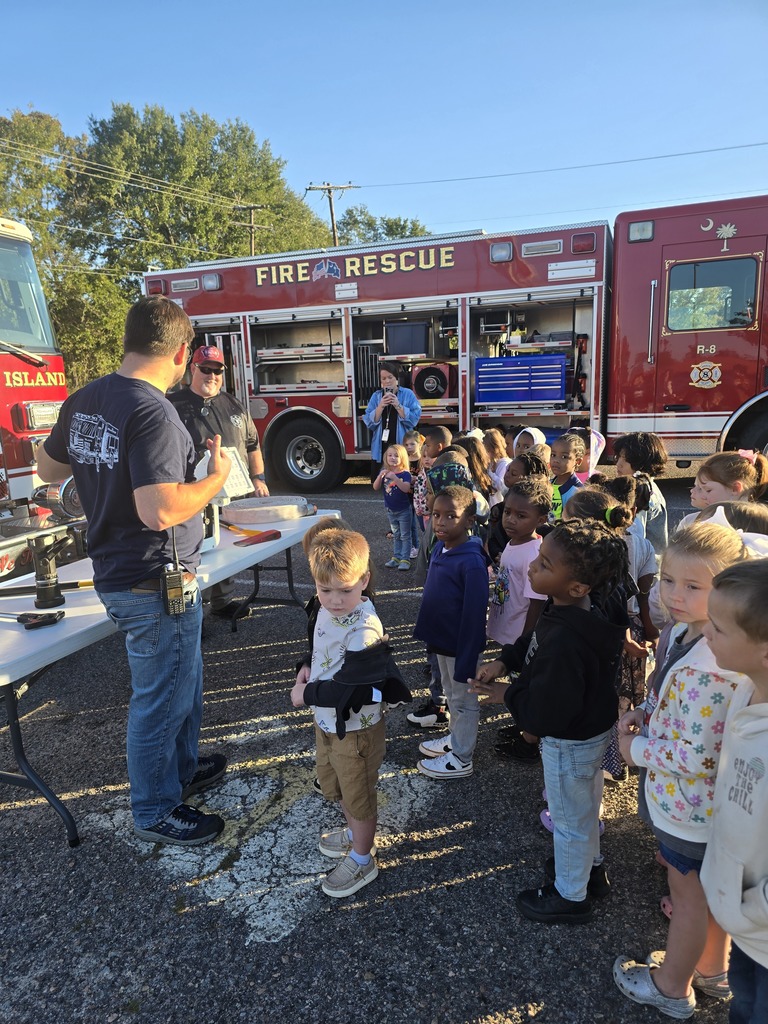 Students and teachers standing in front of fire trucks and firemen.