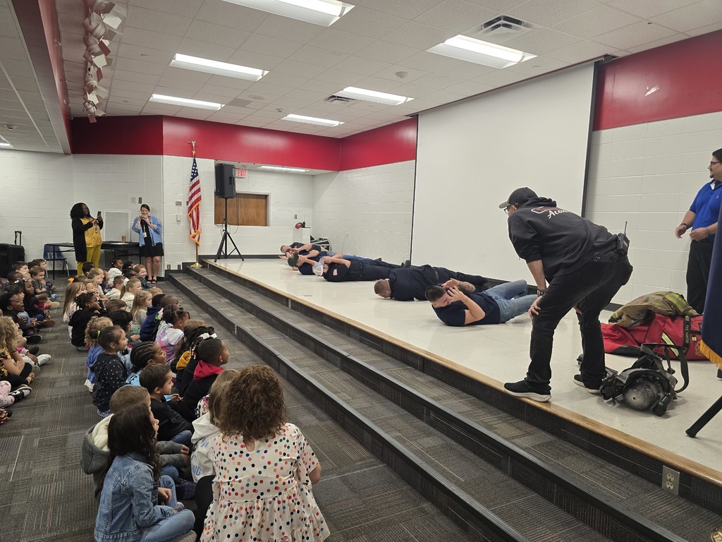 Firemen rolling on stage in front of students.