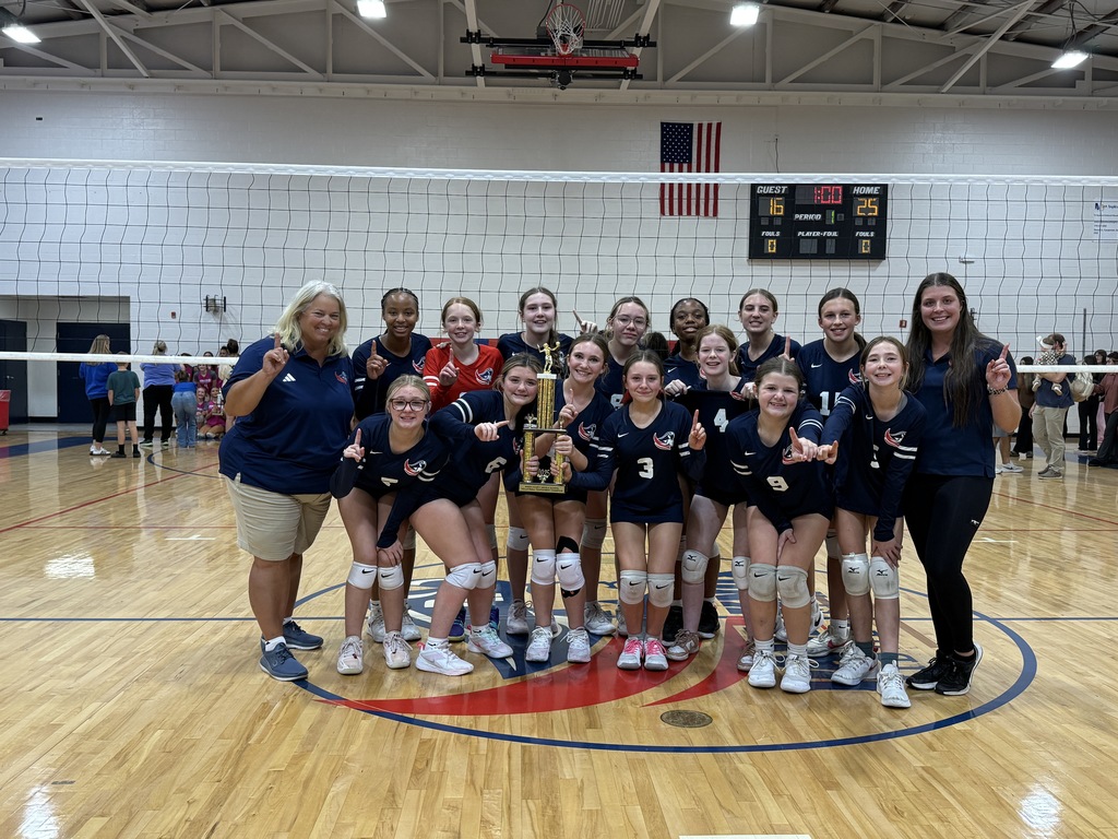 A girls volleyball team poses with a trophy.