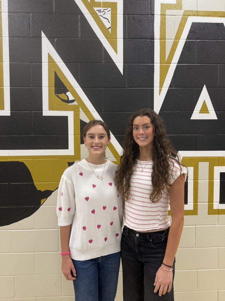 Two female students smiling  in front of jacket wall. 