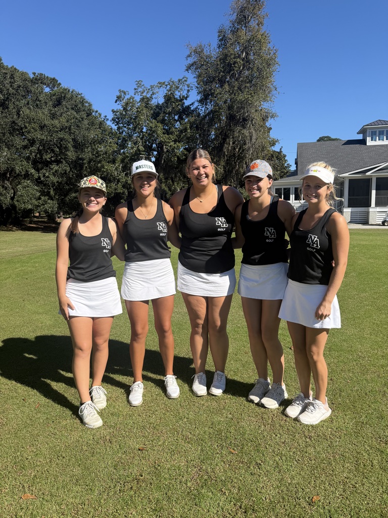 Lady Golfers standing on green with club house in back.