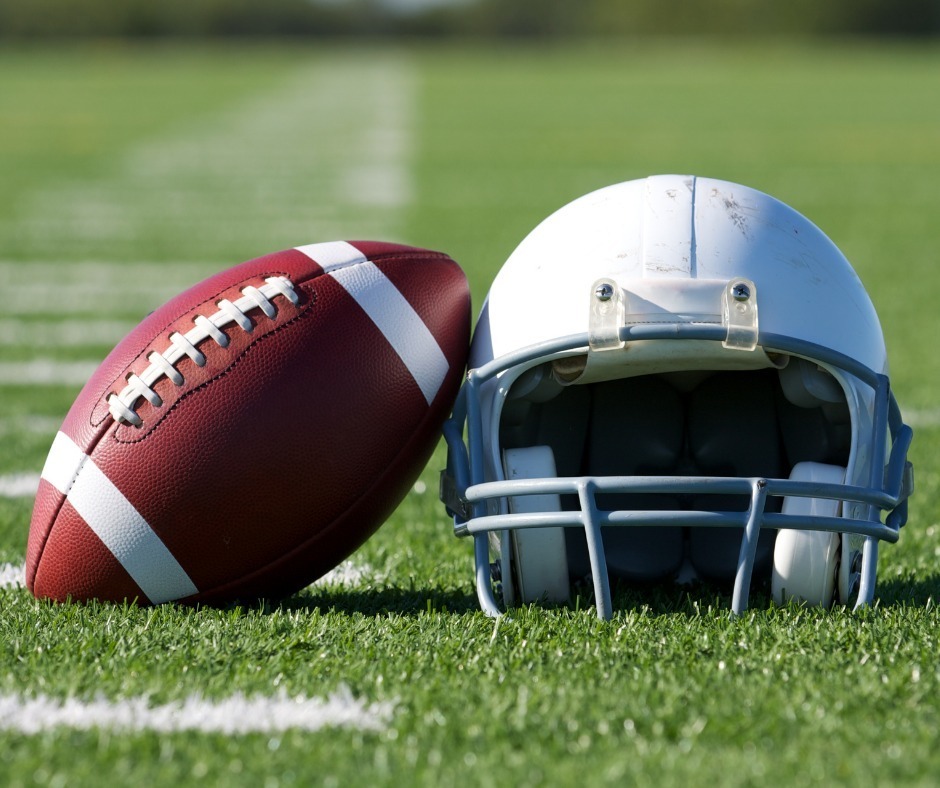 Football propped against a helmet on a football field. 