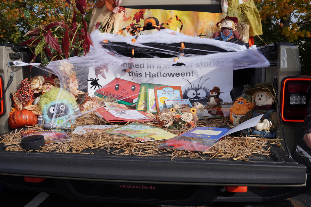 Trunk of truck decorated with straw and pumpkins showcases books for halloween.