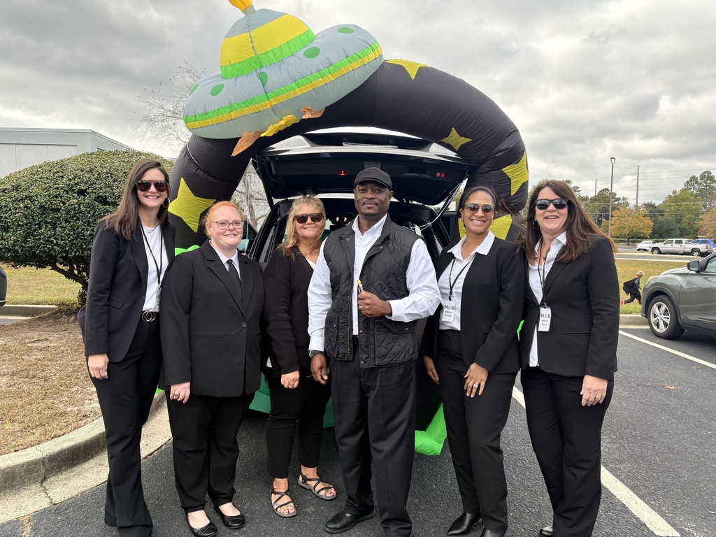 Staff and Superintendent dressed as secret agents posing in front of car decorated with spaceships.