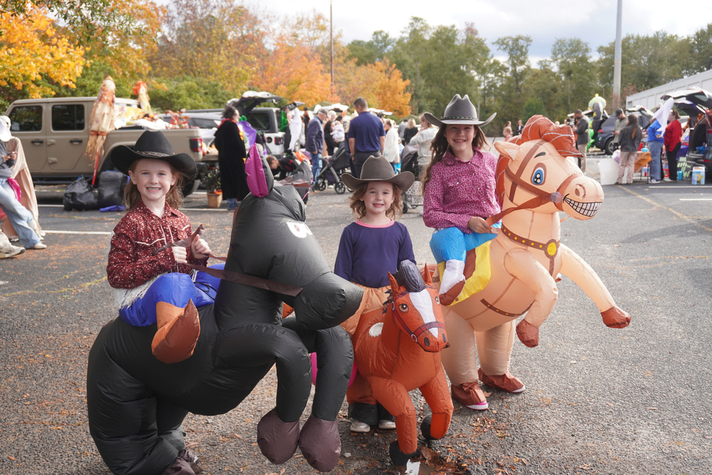 Three young students dressed up as cowgirls with horses.