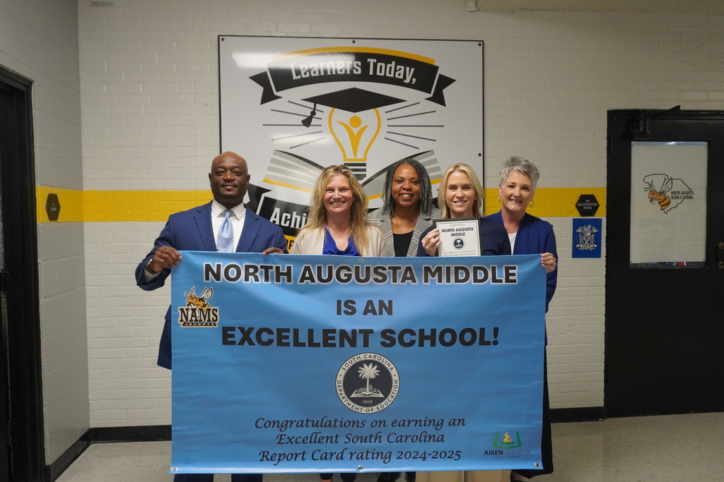 District Leadership and North Augusta Middle current and former principal posing with NAMS Excellent School banner.