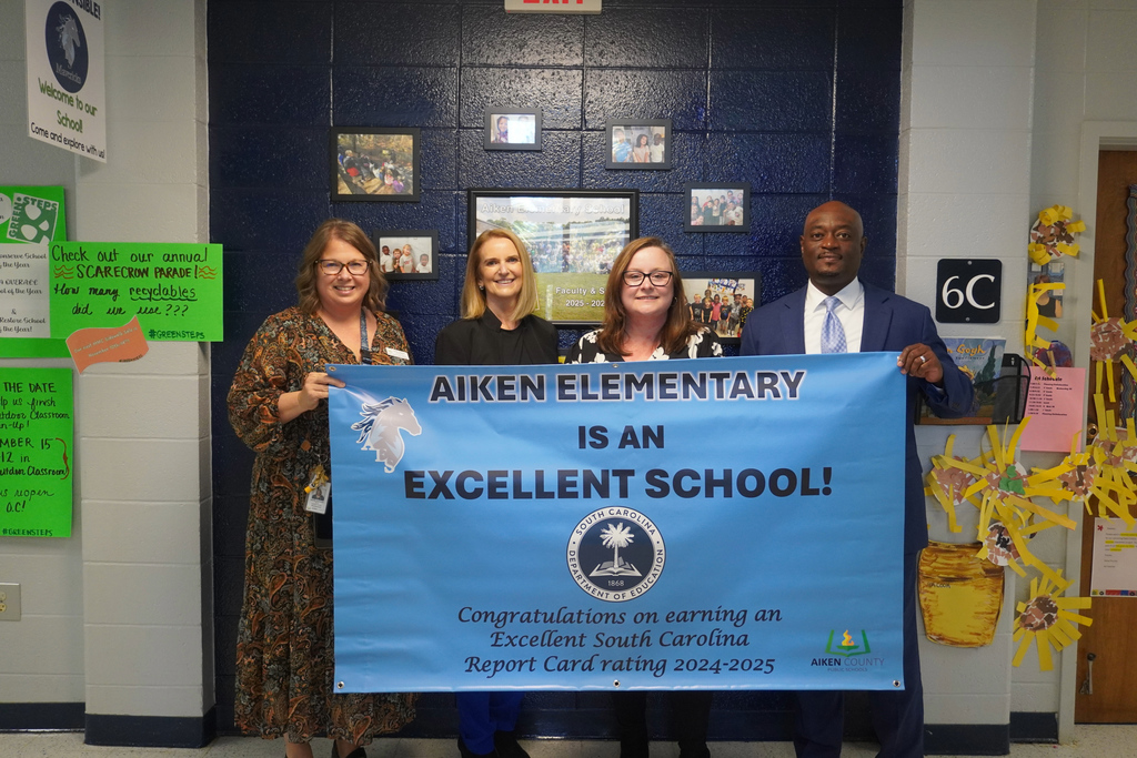 District staff and Aiken Elementary  team posing with Excellent School Report Card Banner. 