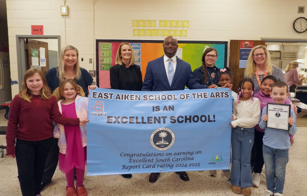 District Leadership, East Aiken School of the Arts leadership and students posing with school's Excellent banner.