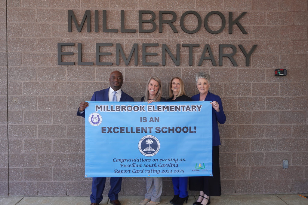 District staff and Millbrook Principal posing with Excellent School Report Card Banner. 