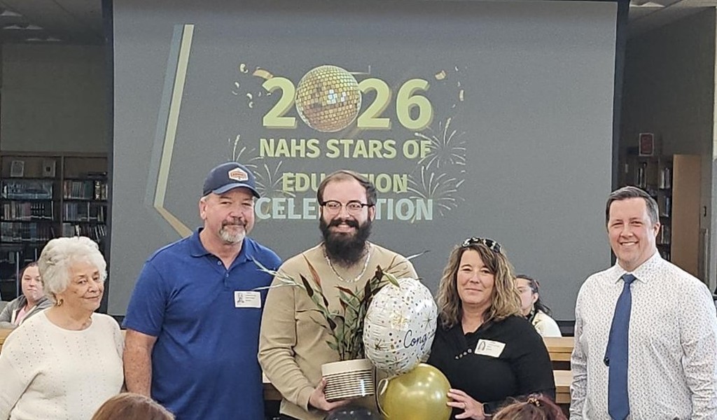 Teacher and family posing in front of sign of 2026 Stars of education.