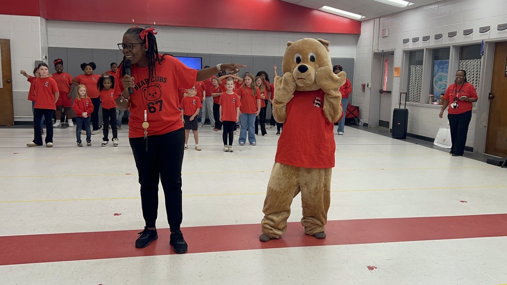 Teacher and bear mascot in front of audience.