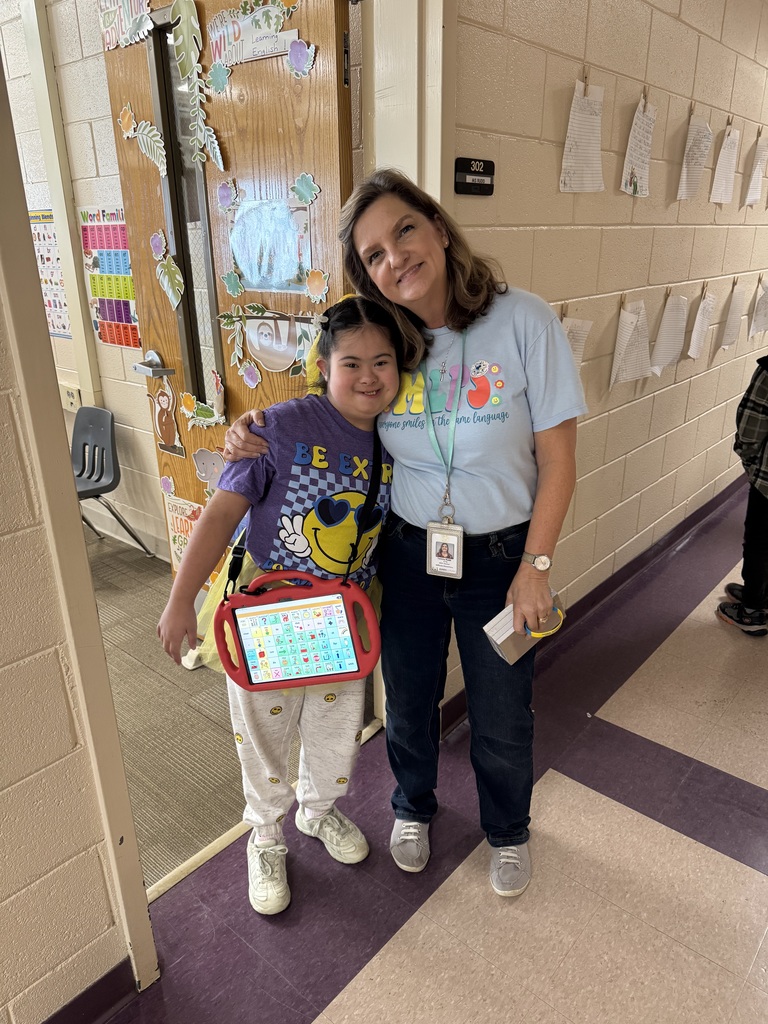 A teacher stands with her arm around a girl smiling.