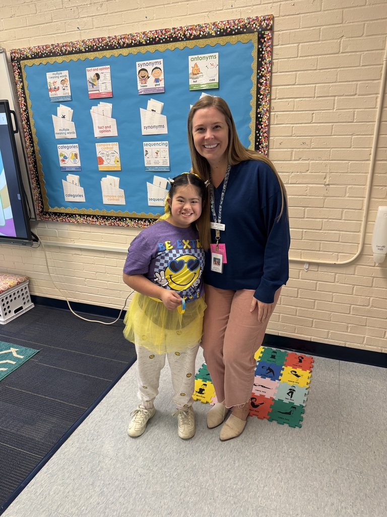 A teacher stands with her arm around a girl smiling.