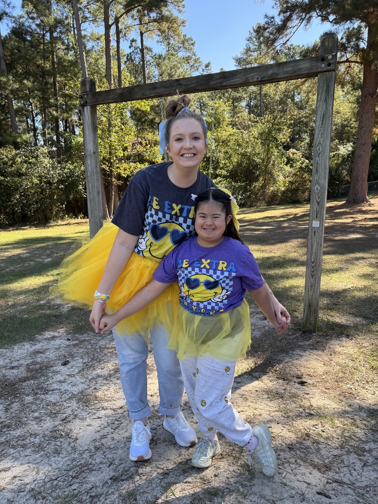 A girl stands in front of a teacher, both are wearing a yellow tutus.