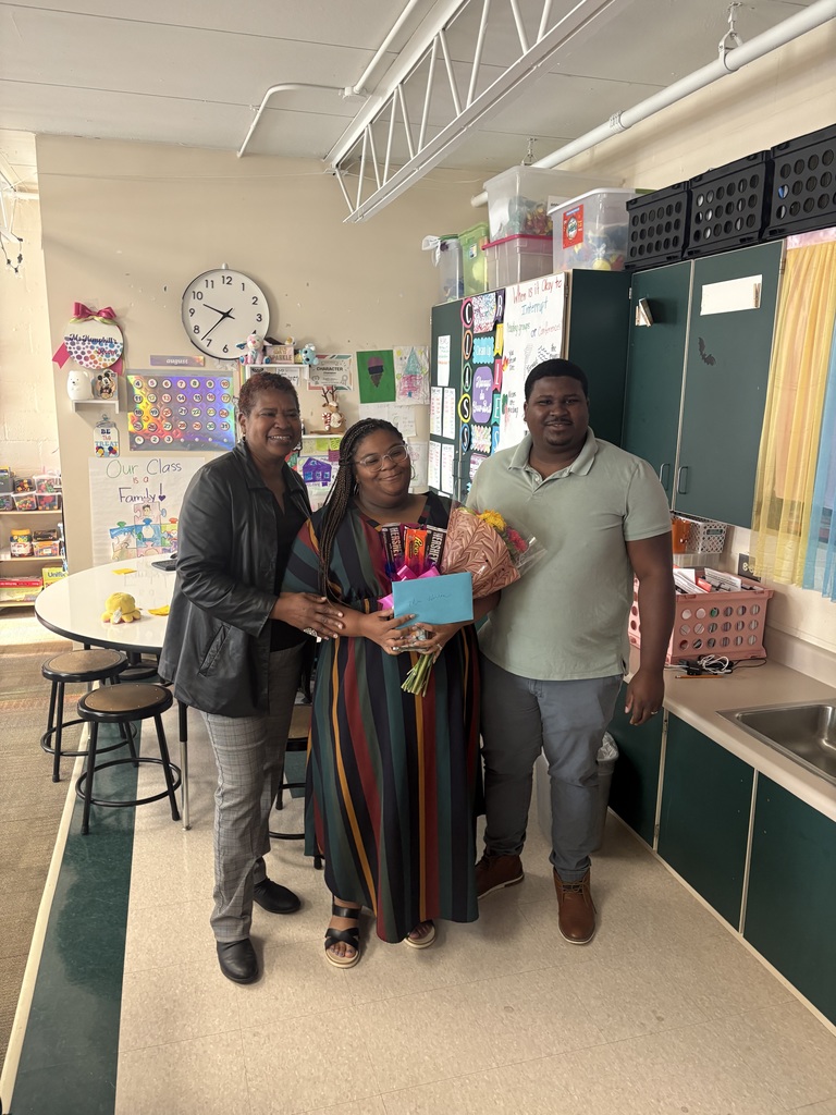A teacher holds a bouquet of flowers and an award and stands in between her mother and her husband.