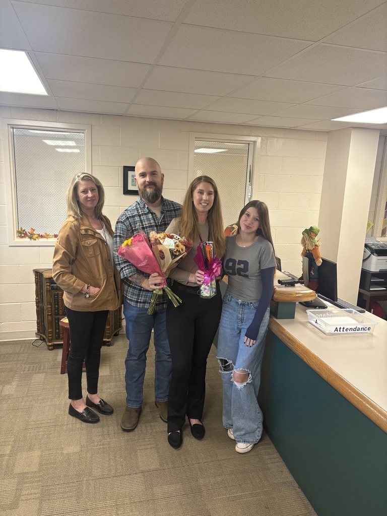 The school secretary holds flowers and an award while standing with two adults and her teenage daughter.