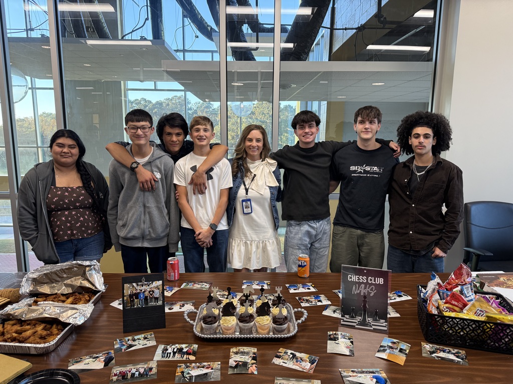 Students and teacher smiling for camera in front of a table full of food. 