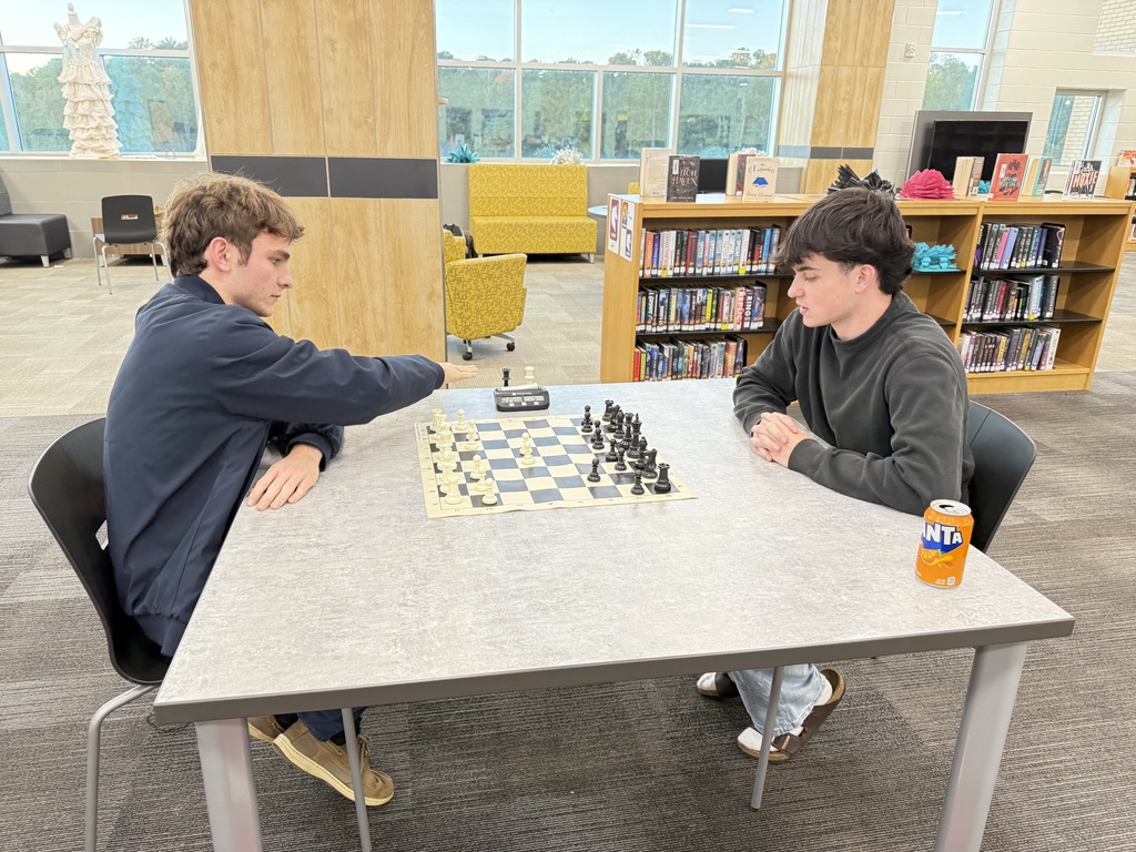 2 Students playing chess in library.