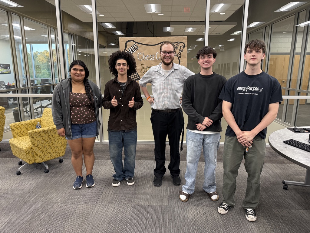 Group of 4 students and 1 teacher smiling for picture in library. 