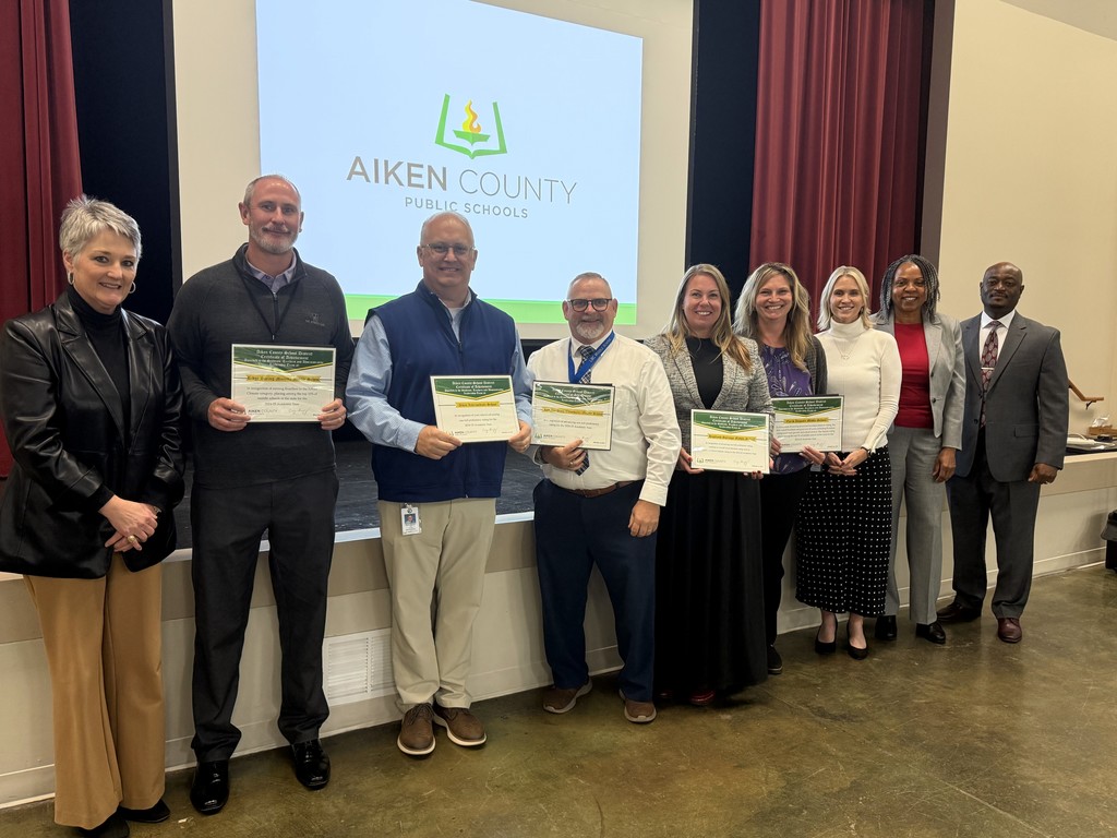 Superintendents stand with school administrators showcasing awards. 