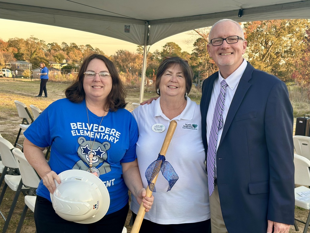 Staff smiling while holding a shovel and hard hats at groundbreaking. 