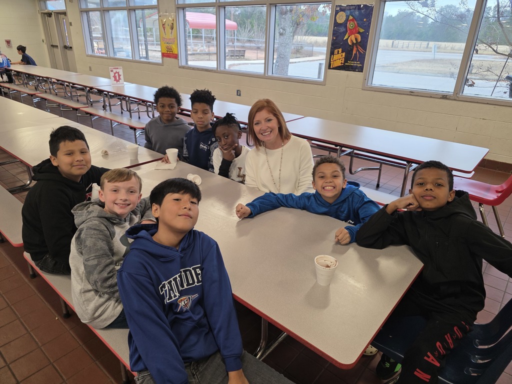 Students drinking hot cocoa at table with principal.