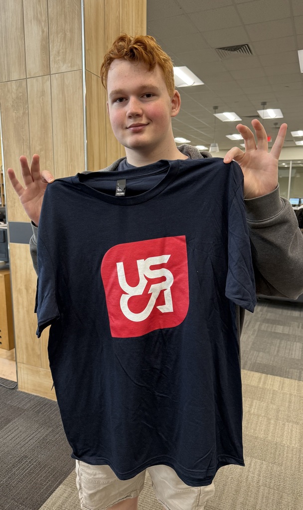 1 Student holding up USCA Shirt in the library,.
