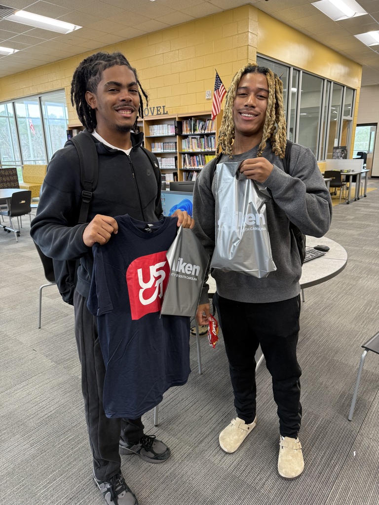 2 Students holding up USCA Shirt in library,. 