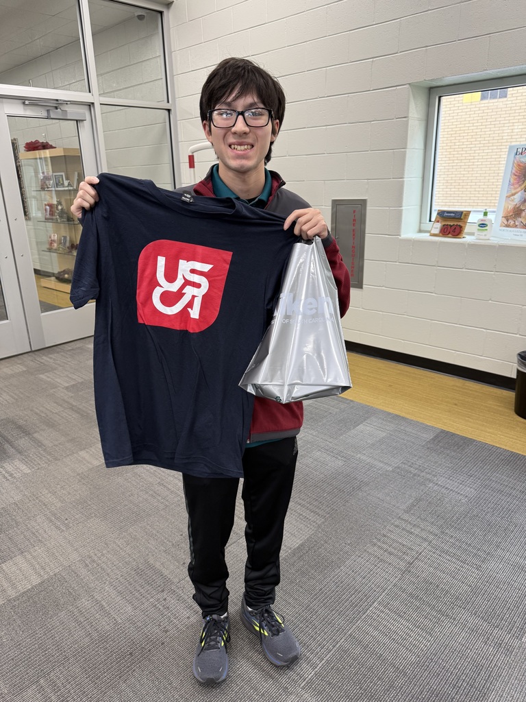 1 Student holding up USCA Shirt in the library,.