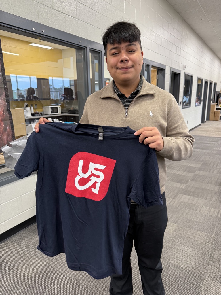 1 Student holding up USCA Shirt in the library,.