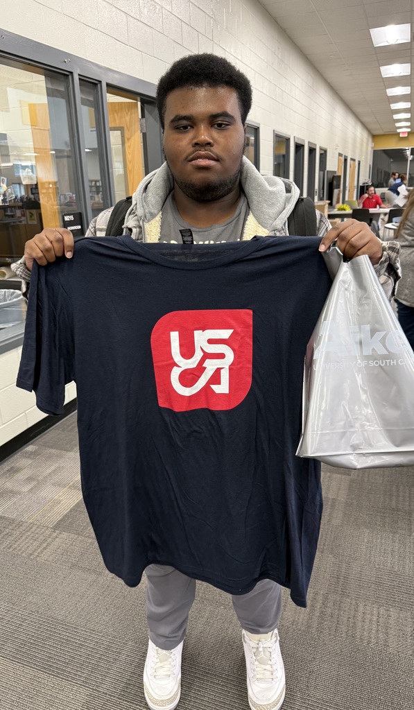 1 Student holding up USCA Shirt in the library,.