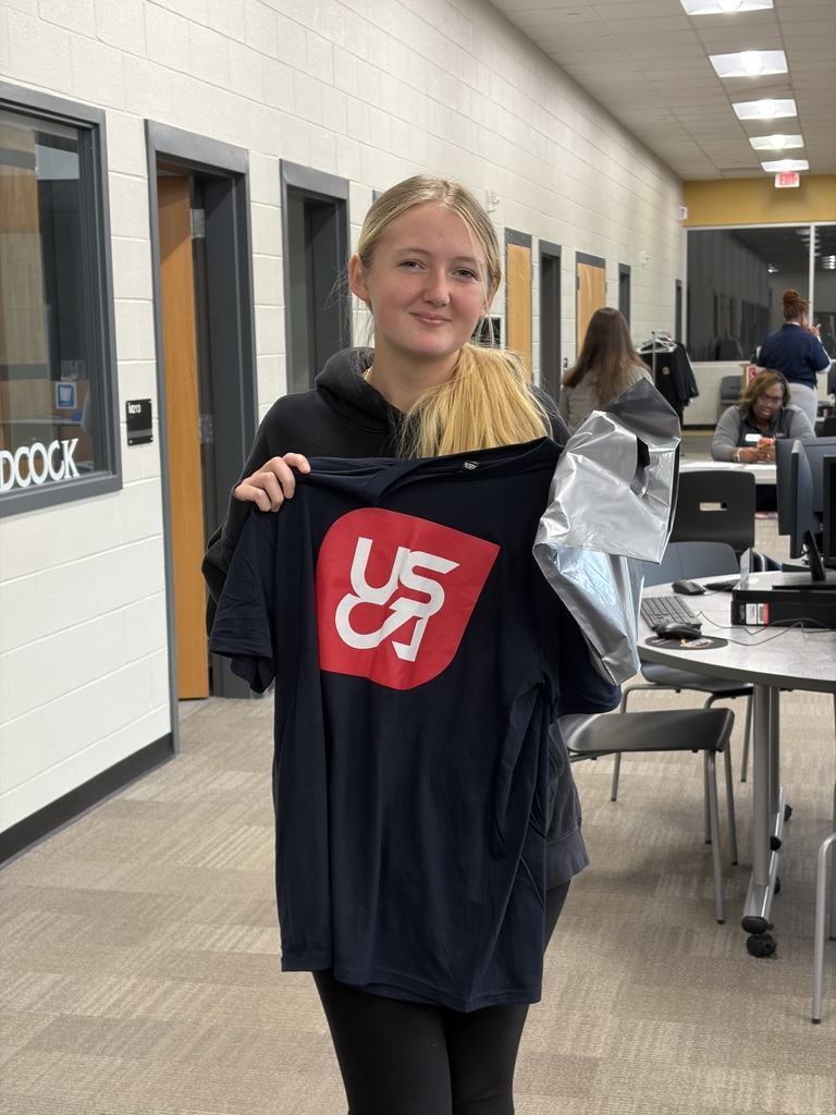 1 Student holding up USCA Shirt in the library,.