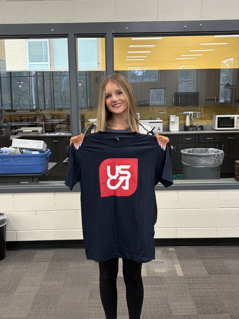 1 Student holding up USCA Shirt in the library,.