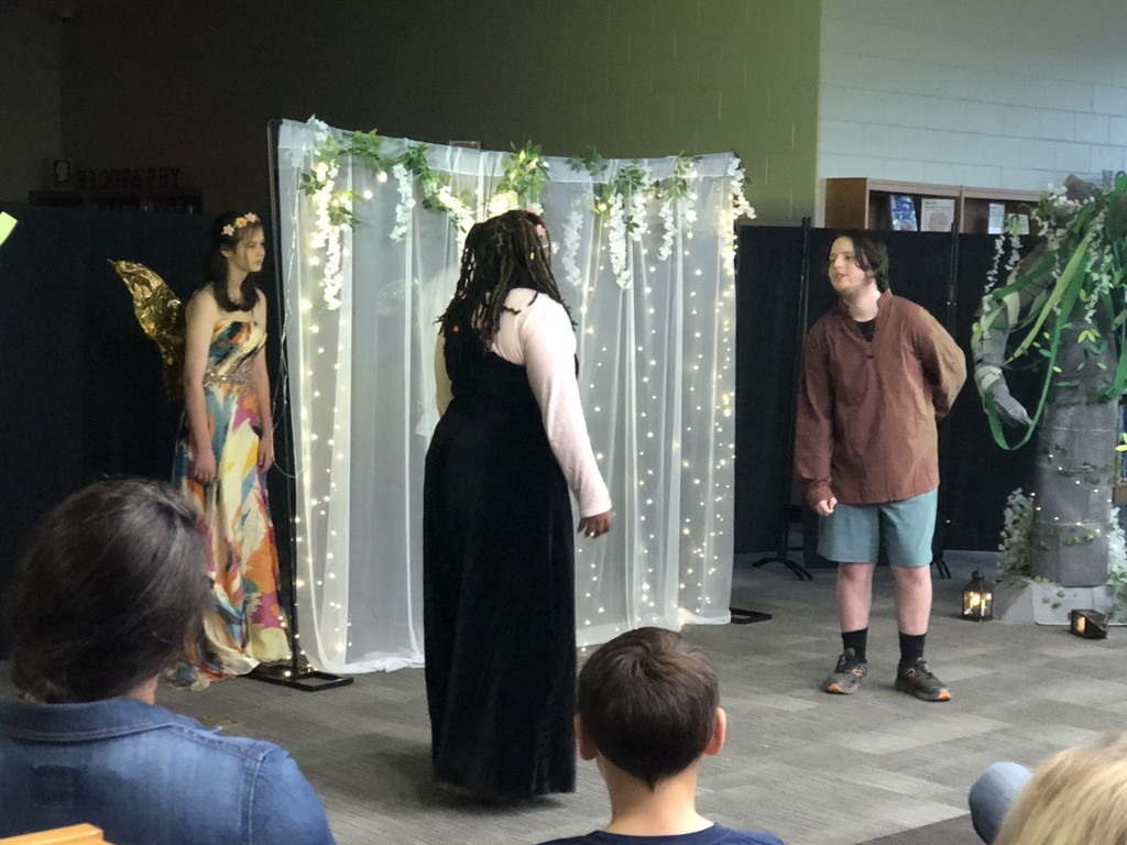 Students in costumes presenting play with sheer lighted backdrop.