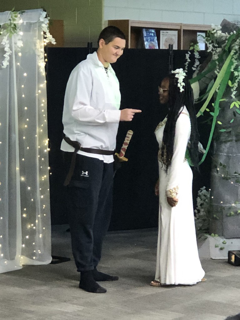 Students in costumes presenting play with sheer lighted backdrop.