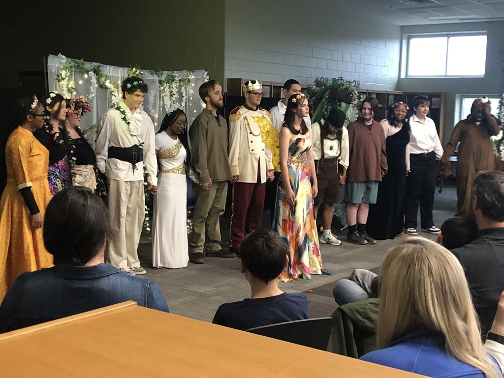 Students in costumes presenting play with sheer lighted backdrop.