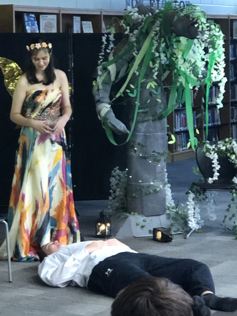 Students in costumes presenting play with tree backdrop.