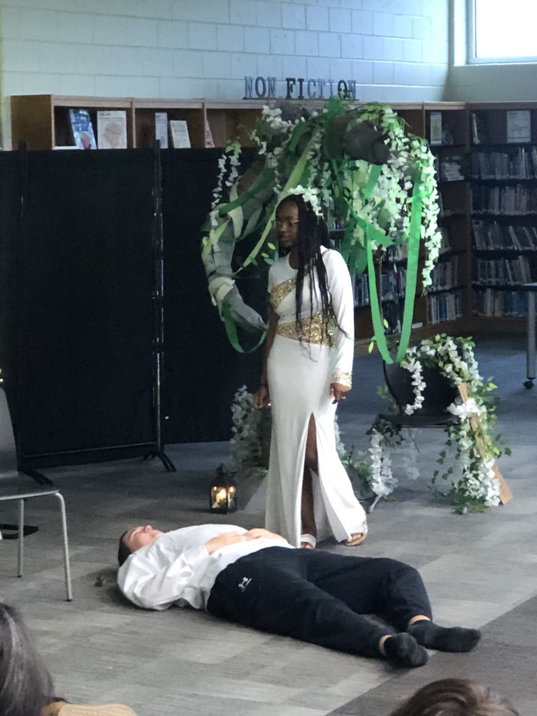 Students in costumes presenting play with tree backdrop.