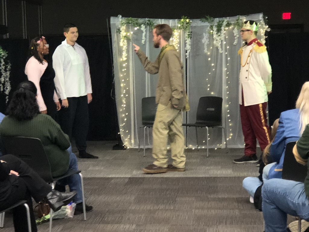 Students in costumes presenting play with sheer lighted backdrop.