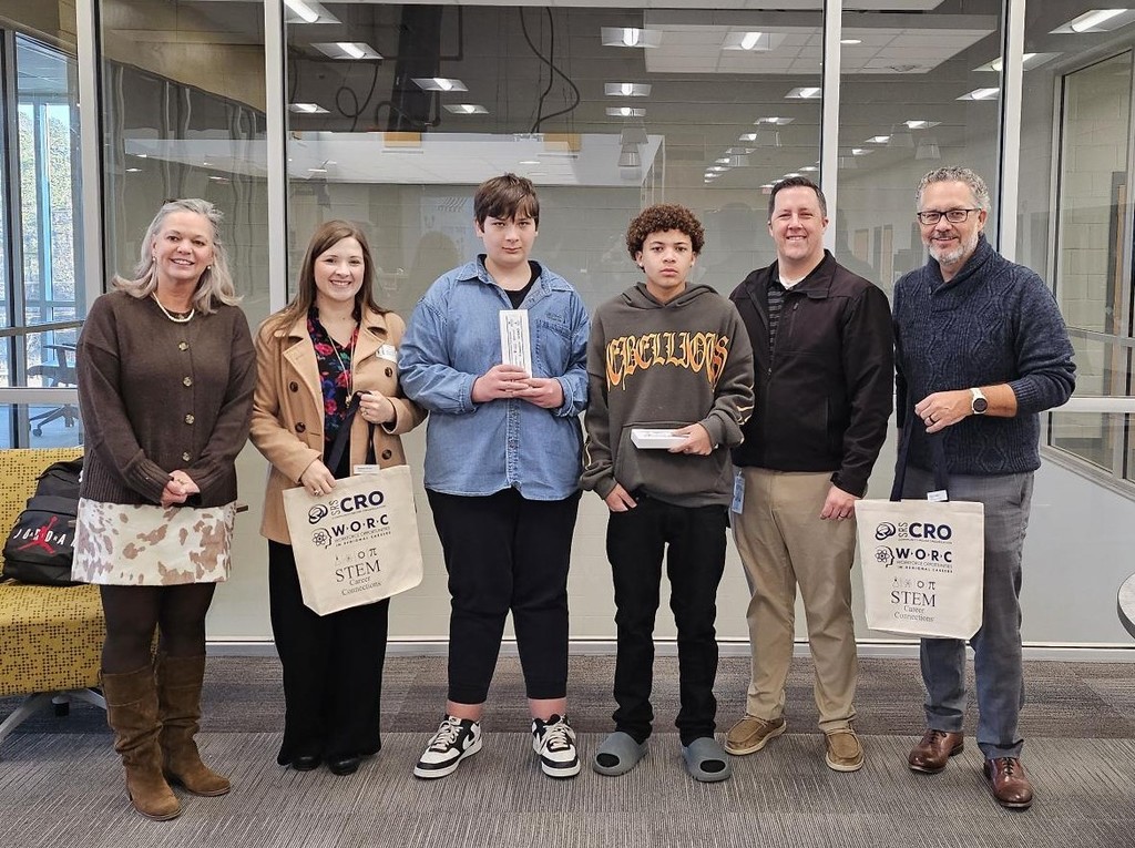 3 Members of SRS CRO, 2 students, and principal standing in front of windows holding CRO bags. 