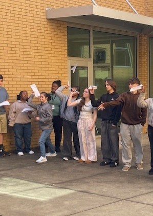 Students flying paper airplanes in courtyard. 