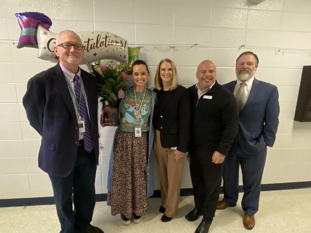 Five adults pose for a picture, one female holding balloons. 