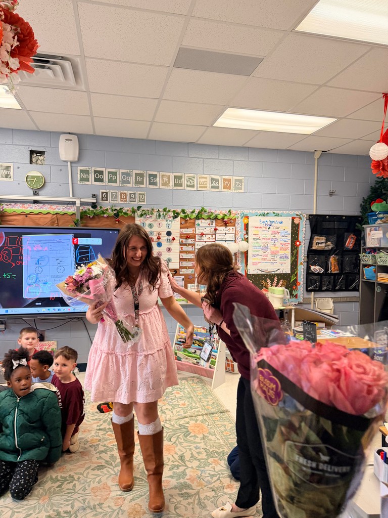 A female adult in a pink dress appears surprised and is holding flowers.
