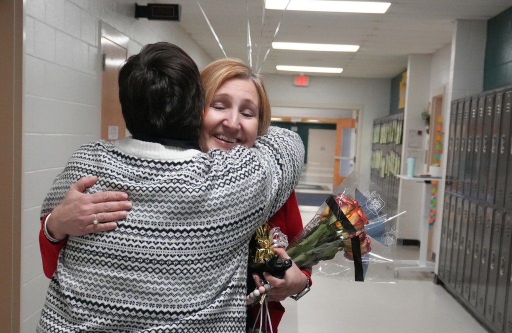 Two women hug in a school hallway.