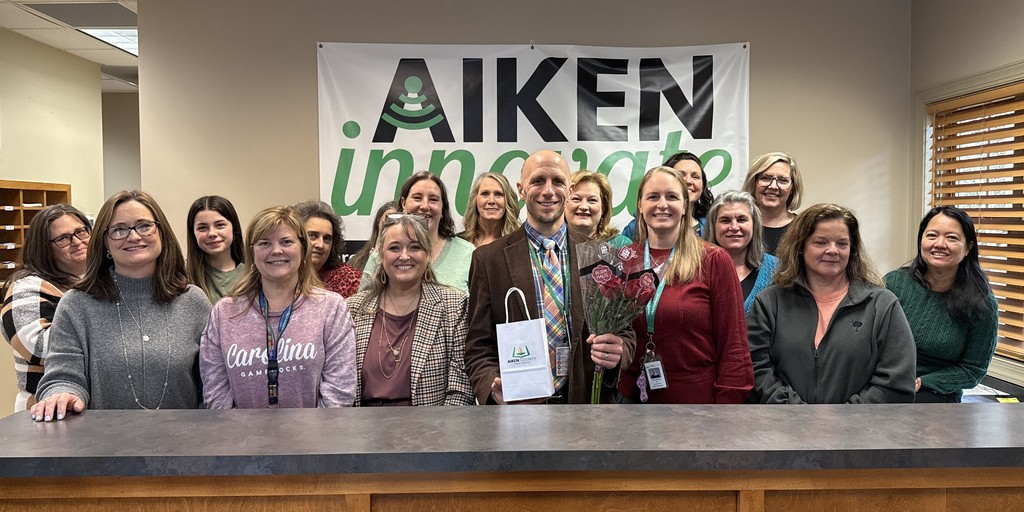 Group of people pose together smiling in front of an Aiken Innovate banner.