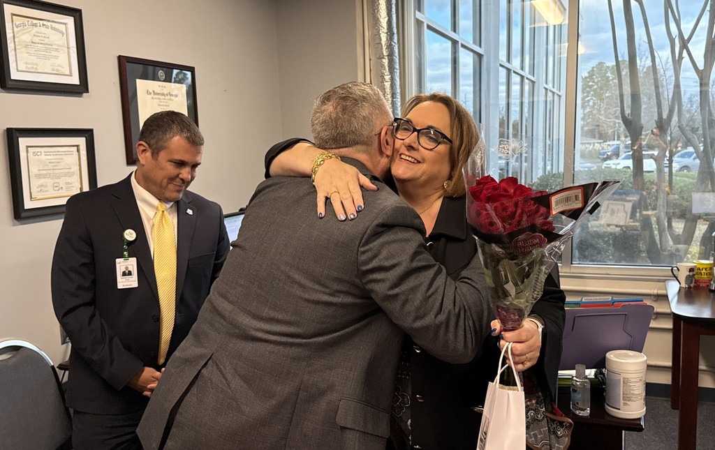 Two people hug in celebration while holding flowers.