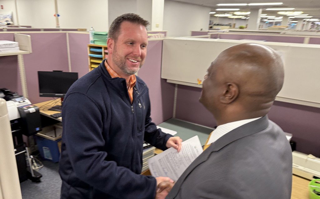 Two men shake hands and smile.